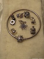 Photo of new Pandora Moments silver bracelet with butterfly clasp surrounded by 8 assorted charms on a beige fabric background.