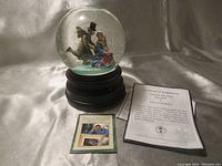 Full view of the snowglobe on black base with certificate of authenticity and informational booklet.