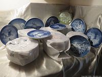 Setup of multiple Royal Copenhagen Christmas plates arranged and some wrapped in foam with year labels visible