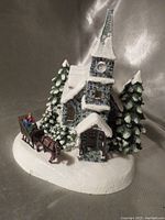 Front and right angled view of the snow-covered church with pine trees and horse-drawn sleigh with rider.