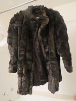 Front view of a black fur jacket hanging on a hanger, showing its texture and length.