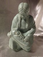 Front view of celadon green pottery sculpture depicting a seated Native American maiden holding her swaddled baby in lap