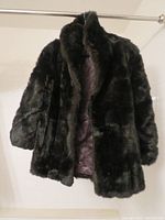 Front view of the black fur jacket showing plush texture and glossy quilted brown lining inside