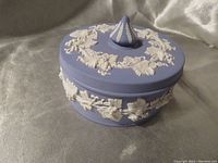 Closed view of vintage matte blue Jasperware trinket box with white floral relief and lid topped with conical knob.