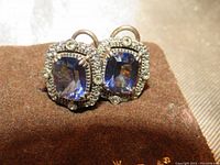 Close-up image of vintage earrings showing square mystic blue stones surrounded by rhinestones, on a brown fabric background.