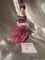 Photo of the vintage Josef Originals porcelain figurine of a woman sitting reading a book dressed in a purple gown with floral details.