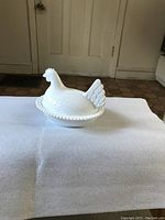 Full view of the white milk glass hen dish with lid on a white surface, showing overall shape and texture.