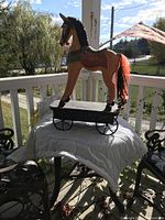 Wooden antique toy horse with black mane and orange textured tail on wheeled black platform outdoors on porch table.