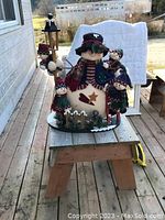 Large snowman Christmas decoration with three smaller snowmen, placed on a wooden sawhorse outside.