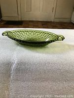 Green carnival glass dish with textured diamond pattern and two handles, displayed on a white surface with a neutral background