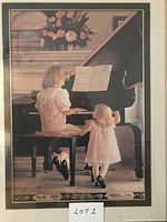 Framed signed print showing two young girls at piano in warm indoor setting.