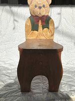 Front view of wooden child's chair showing bear-shaped backrest hand painted in warm tones with red bow tie and green vest.