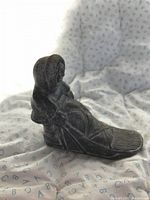 Photo showing a dark stone carving of an Inuit figure in traditional clothing holding a wolf, with detailed textures on the hood and boots, placed on a fabric background.