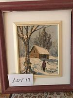 Framed oil painting showing a winter landscape with a cabin, a large tree, and a person in a red jacket walking with a bag in the snow.