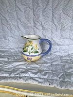 Photo of medium-sized ceramic jug with floral and butterfly patterns, showing the side with handle and decorations.