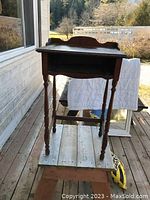 Small solid wood table or desk outdoors, showing front and side views of the turned legs and open shelf