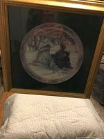 Framed collector plate featuring a winter scene with two women in period clothing riding a horse-drawn sleigh through a snow-covered landscape, mounted in wooden frame with black matte.