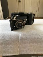 Vintage folding bellows camera photographed from front angle showing lens and bellows fully extended