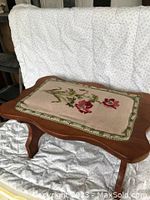 Front view of vintage wooden footstool with needlepoint floral top showing detailed needlework and wood finish.