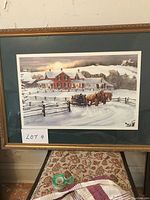 Framed winter scene print featuring a red brick house and horses pulling a log-loaded sleigh in snow.