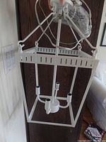 Full view of white metal chandelier light fixture with four arms for bulbs, showing hanging rods and ceiling mount.