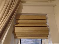 Blinds partially raised showing beige linen-look fabric and horizontal fold pleats.