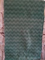 Full view of one green cotton chenille rug showing the overall chevron zigzag pattern and size relative to background.