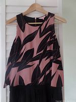 Front view of the jumpsuit showing sleeveless rose and black patterned top with hanger and plain black pants below