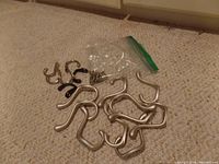 Photo showing all metal coat hooks arranged on carpet including larger silver hooks and smaller black hooks with a clear plastic bag containing screws.