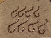 Image showing eight brushed silver/chrome metal coat hooks laid out on a carpeted surface, all identical in shape and size