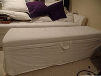Side view of the white rectangular storage ottoman with removable fabric cover, showing the length and handle on front.