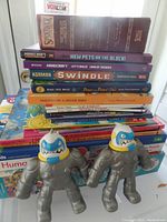 Photo showing stacked kids' books, puzzle books, and two shark-headed action figure toys on top.