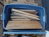Top down view of open blue plastic tote filled with assorted wood stakes and wood boards.
