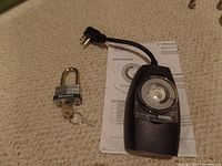 Outdoor timer and Master padlock with keys placed on carpet with instruction sheet underneath the timer