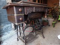Side view of the treadle sewing machine wooden cabinet with wrought iron base showing ornate metalwork and two side drawers.