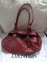 Front view of large red leather Danier handbag with double straps and buckles, on white Danier dust bag.