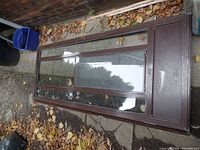Full view of the brown screen door laid on ground, showing its overall condition and size compared to surroundings.