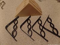 Four black metal shelf brackets with decorative intertwined loops.