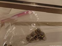 Metal sliding door rollers with mounting brackets in plastic bag on white surface.