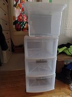 Complete view showing clear plastic filing tote stacked on top of three-drawer plastic storage unit on wheels, taken indoors on wooden floor near furniture.