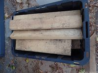 Black plastic tote filled with various lengths of used 2x4 lumber pieces showing weathered and dirty surfaces.