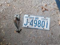 Photo of the front side of a 1966 Ontario license plate and a black metal door handle.