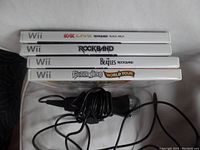 Stack of four Wii game cases with visible titles: AC/DC Live Rockband Track Pack, Rockband, Beatles Rockband, Guitar Hero World Tour, with a wired microphone on top.