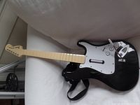 Full view of black Wii Rock Band guitar controller showing front with beige fretboard and strap.