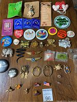 Wide view of assorted pins, brooches, and buttons laid out on wood surface including animal shapes, novelty buttons, and various lapel pins.