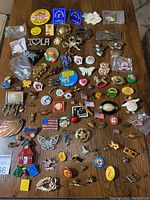 Overview of multiple buttons, brooches, and pins spread out on wooden surface showing variety of styles and colors.