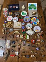 Various vintage to current pinned buttons, brooches, and lapel pins displayed on a wooden surface including holiday and novelty themed pieces.
