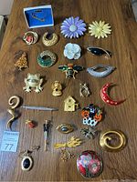 Photo showing various vintage to current buttons, brooches, and lapel pins arranged on a wooden surface, including floral, animal, abstract, and holiday-themed designs.