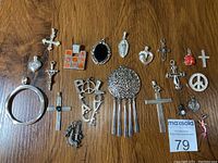 Top view of all silver toned charms and pendants laid out on wooden surface showing variety of designs and shapes including crosses, hearts, peace signs, and decorative pendants.
