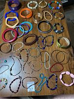Full view of 40 assorted costume jewelry bracelets including bangles, beaded, and stretch styles in various colors and materials spread on a wooden surface.